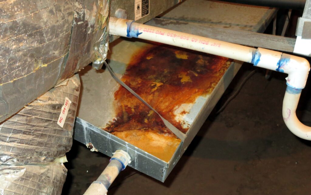 Photo of rust inside an A/C overflow tray inside an attic.