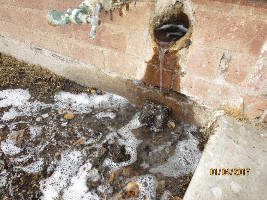 Photo of water leaking from a sewer cleanout on the side of a house.